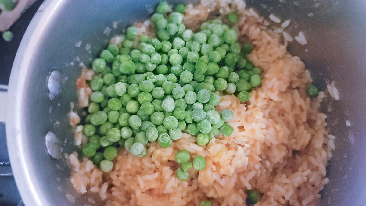 Adding peas to the cooked rice.