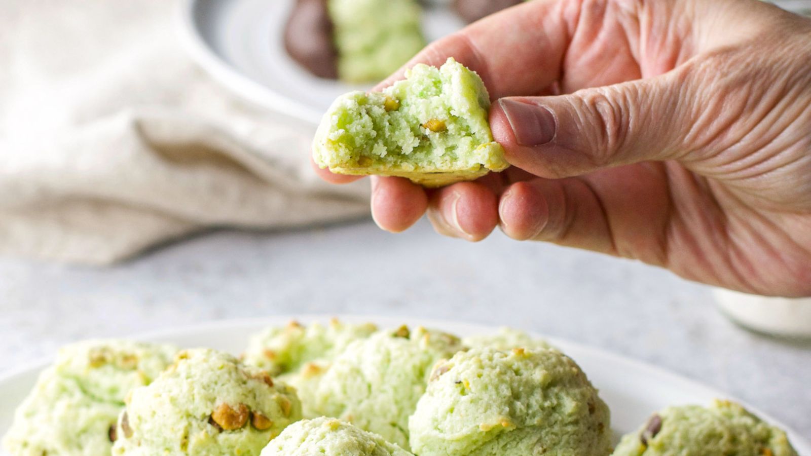Woman's hand with a bite taken out of a pistachio cookie.