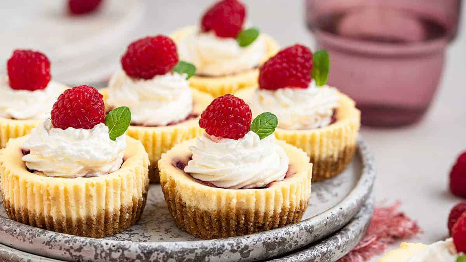 Mini Cheesecakes with whipped cream and a fresh raspberry on top.