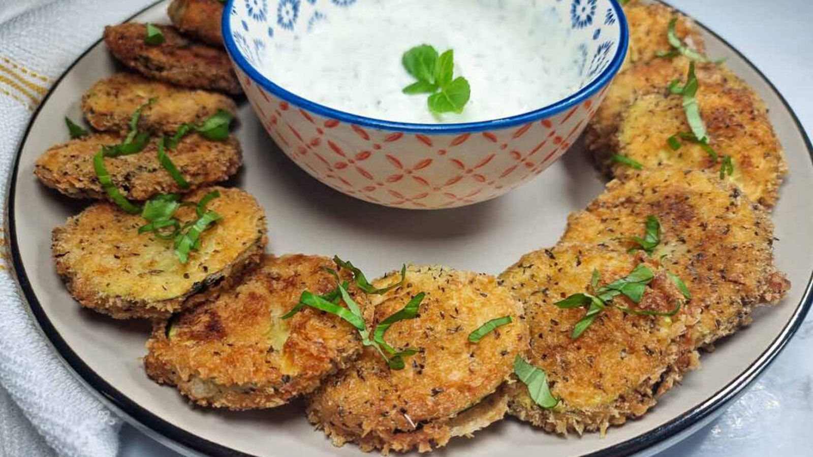 Fried zucchini rounds surrounding a bowl of dip.