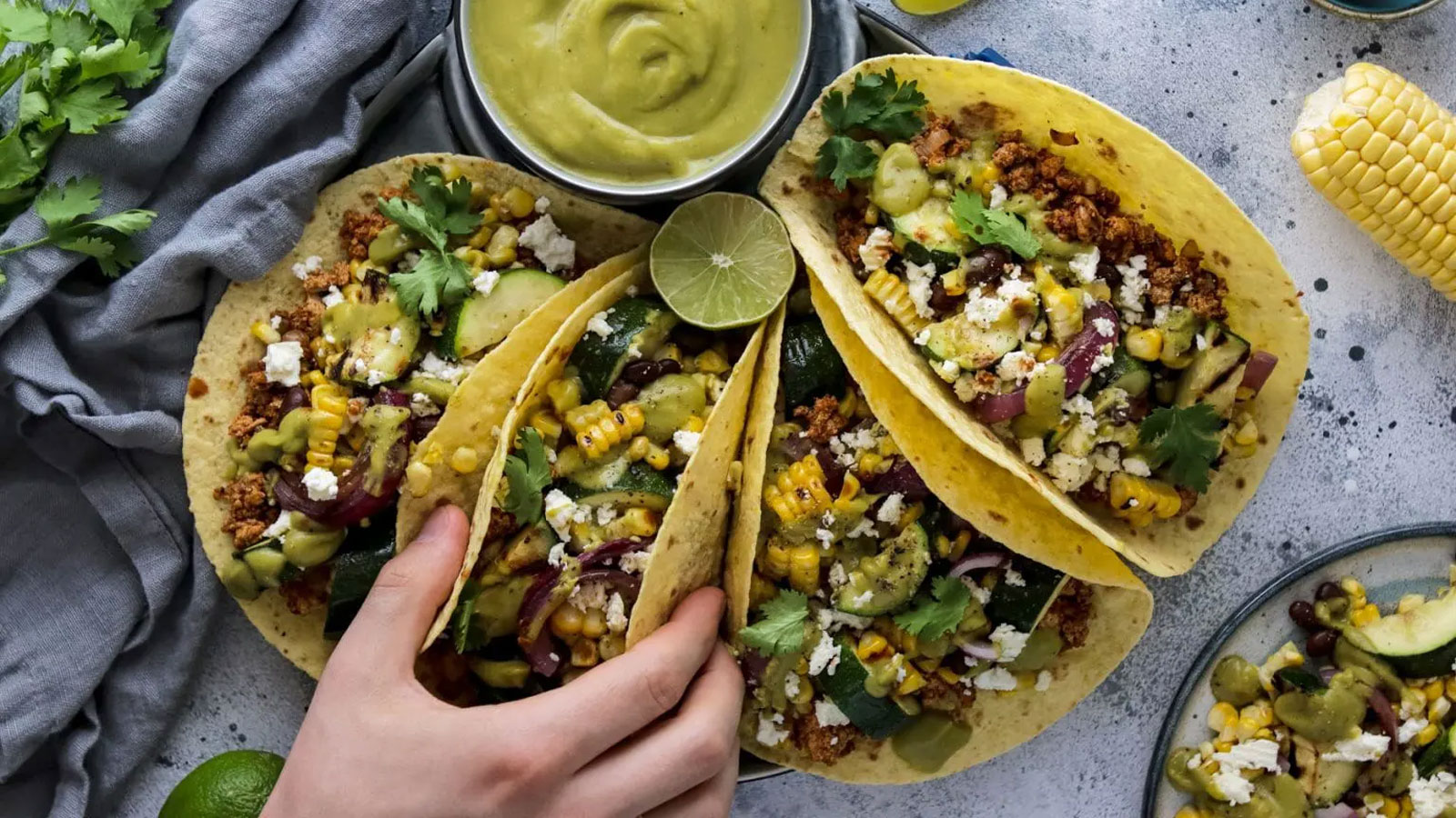 Four tacos on a plate with sauce.
