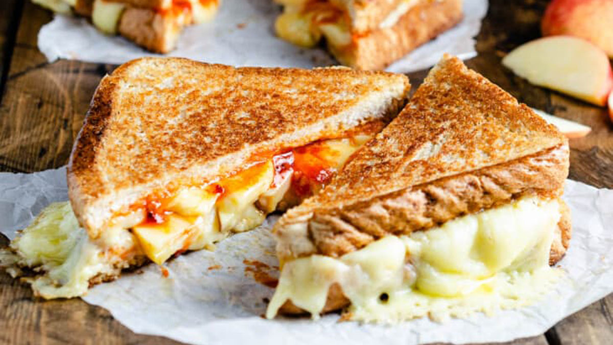 Grilled cheese with sliced apple an hot sauce on a white paper.
