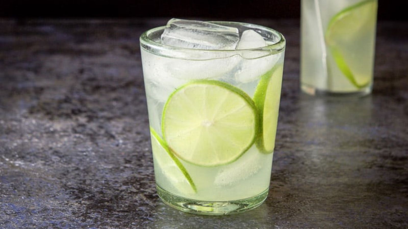 Gin lime cocktail in a glass with sliced limes.