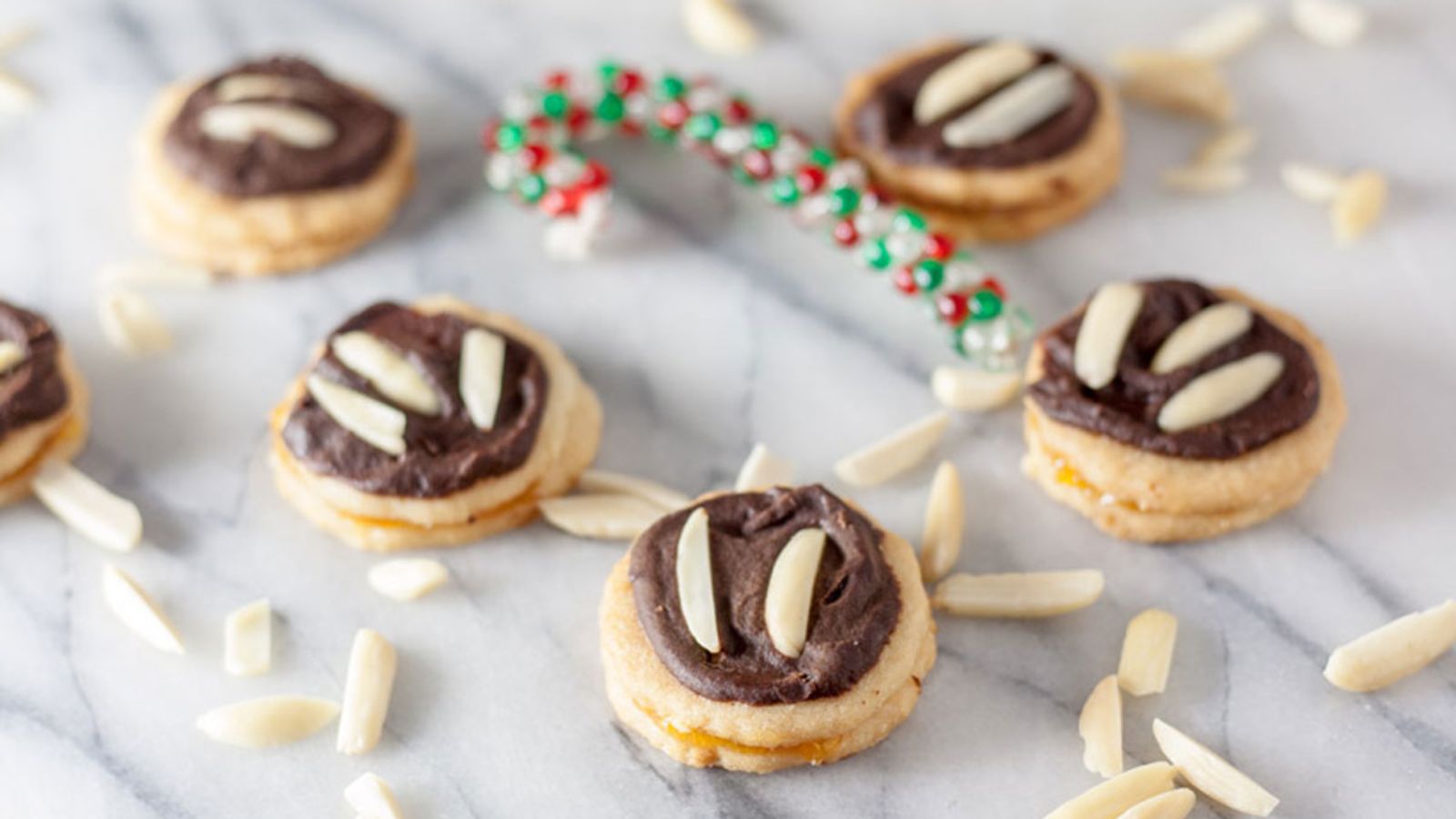 Chocolate covered Ischelers Tortellettes Sandwich Cookie with slivered almonds on marble board.
