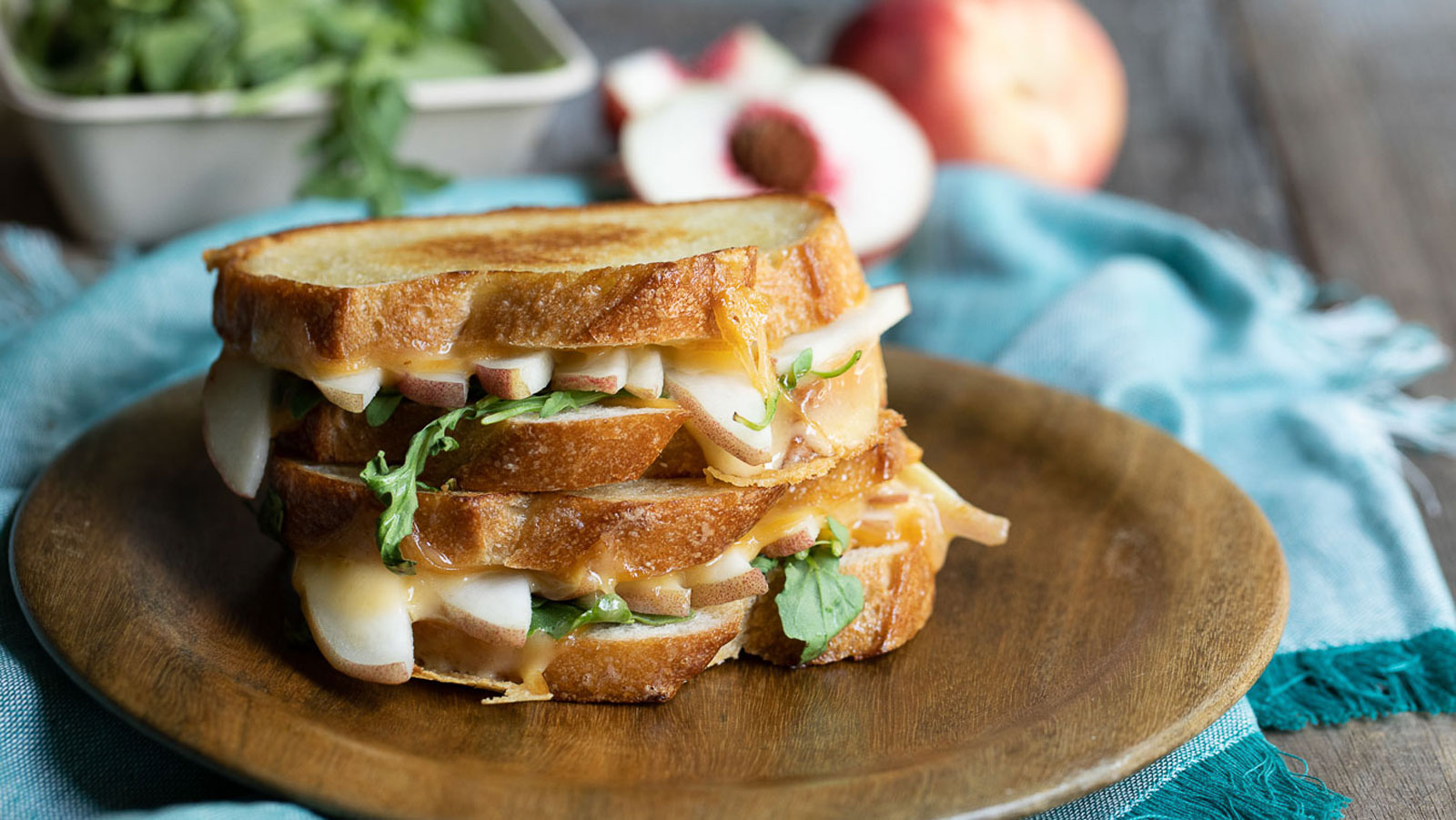 Sliced peaches and arugula on a grilled cheese on a wooden board.