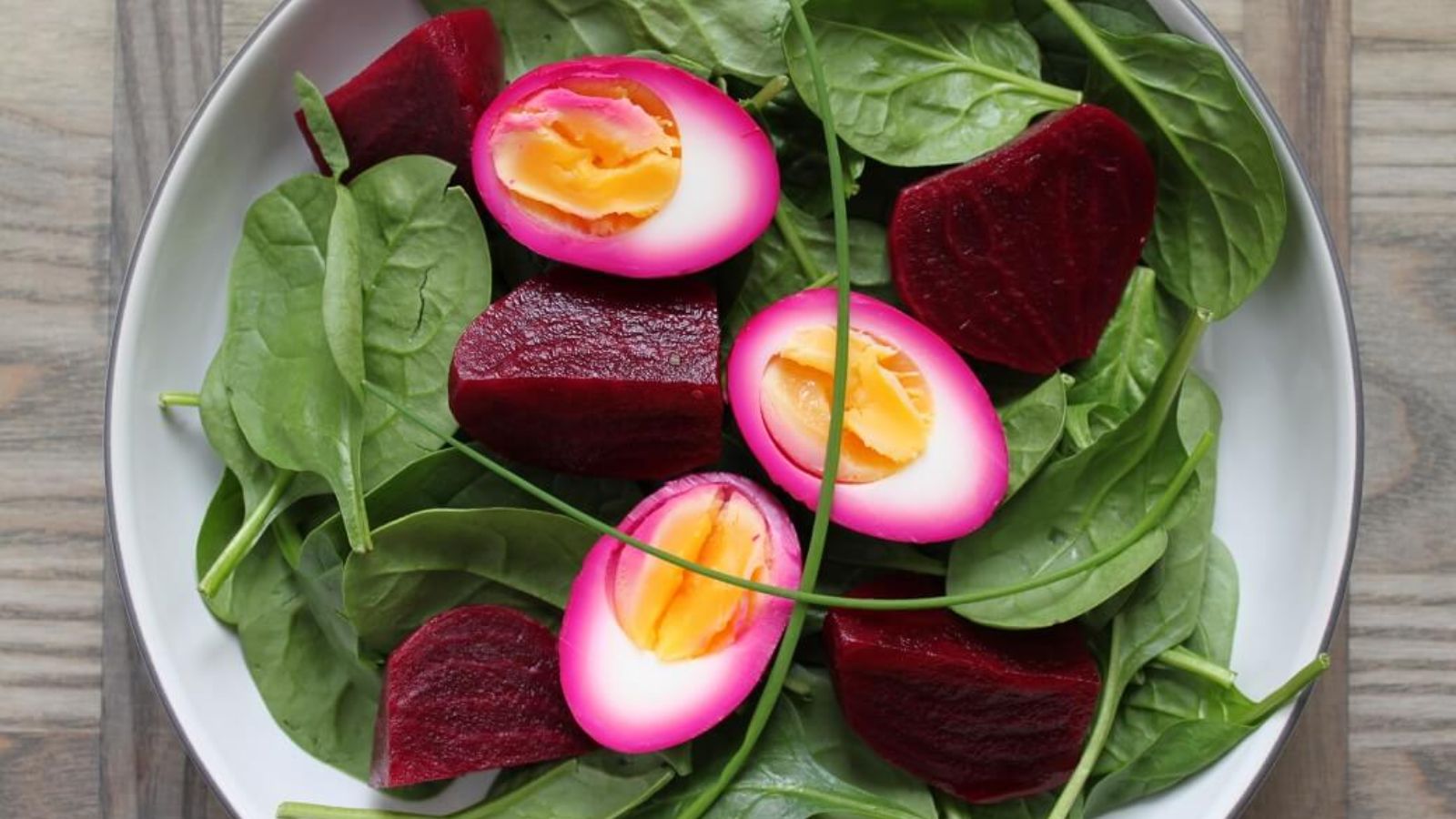 Spinach salad with beet pickled eggs on a plate.