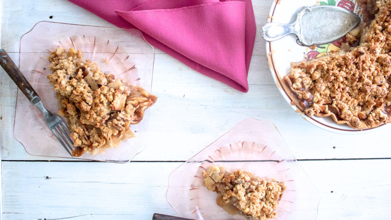 Pieces of apple pie on pink glass plates with the whole pie in a pie tin.