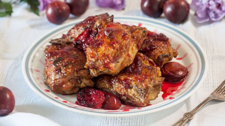 Chicken piled on a plate with grilled plums.