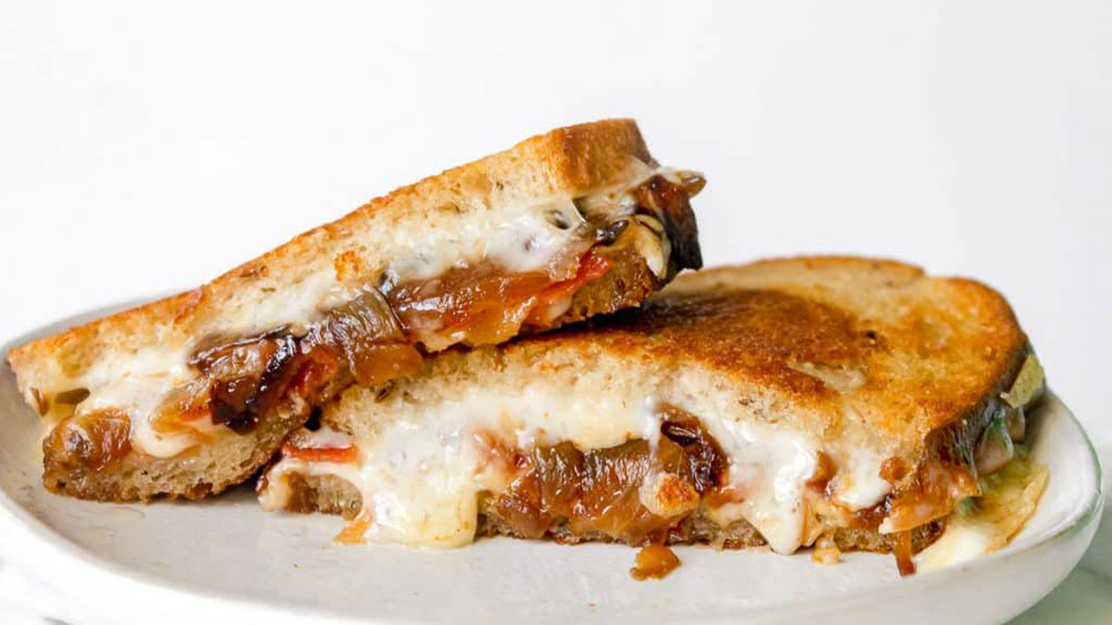 Grilled cheese sliced in half showing bacon and caramelized onions.