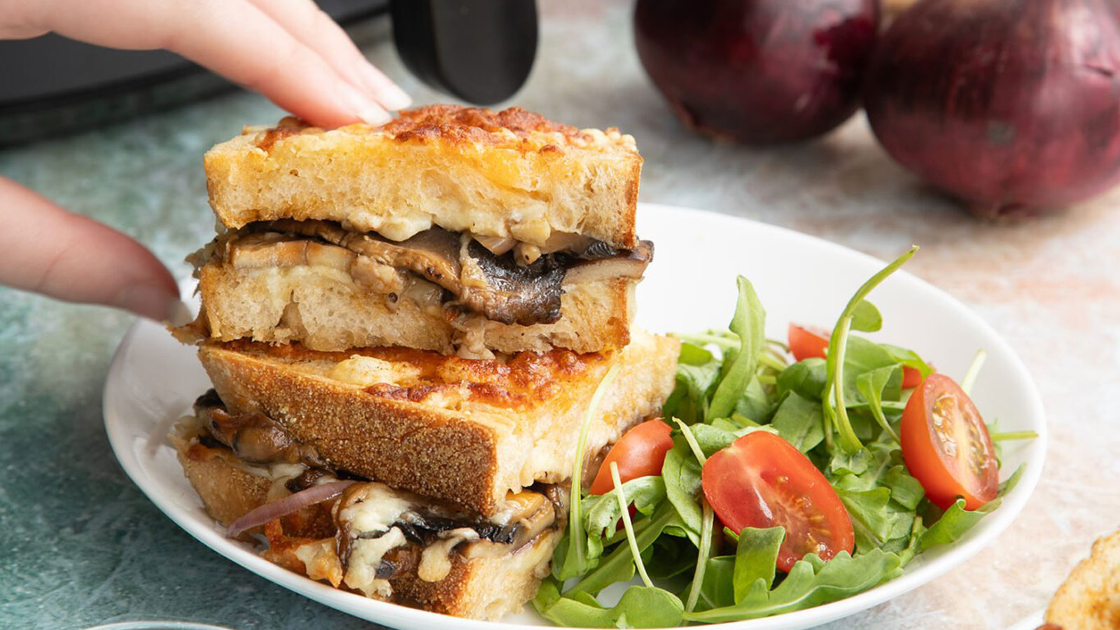 Woman's hand grabbing a mushroom and cheese sandwich.