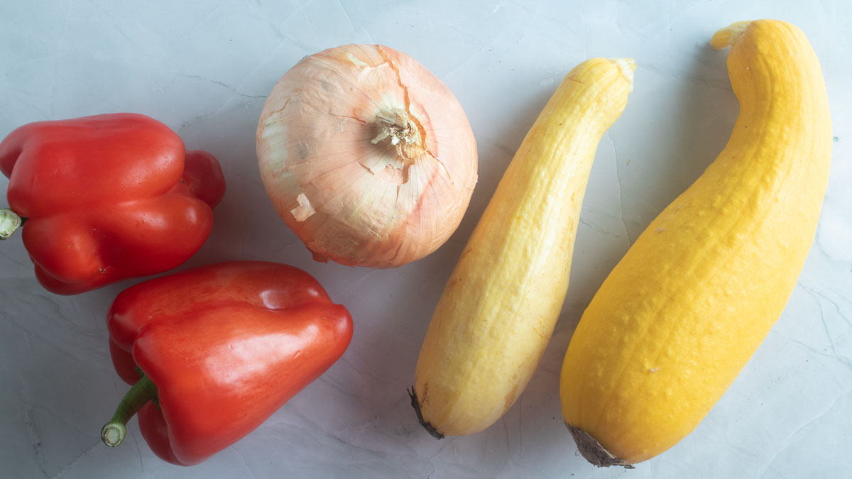 Squash, onion and red peppers on a board.