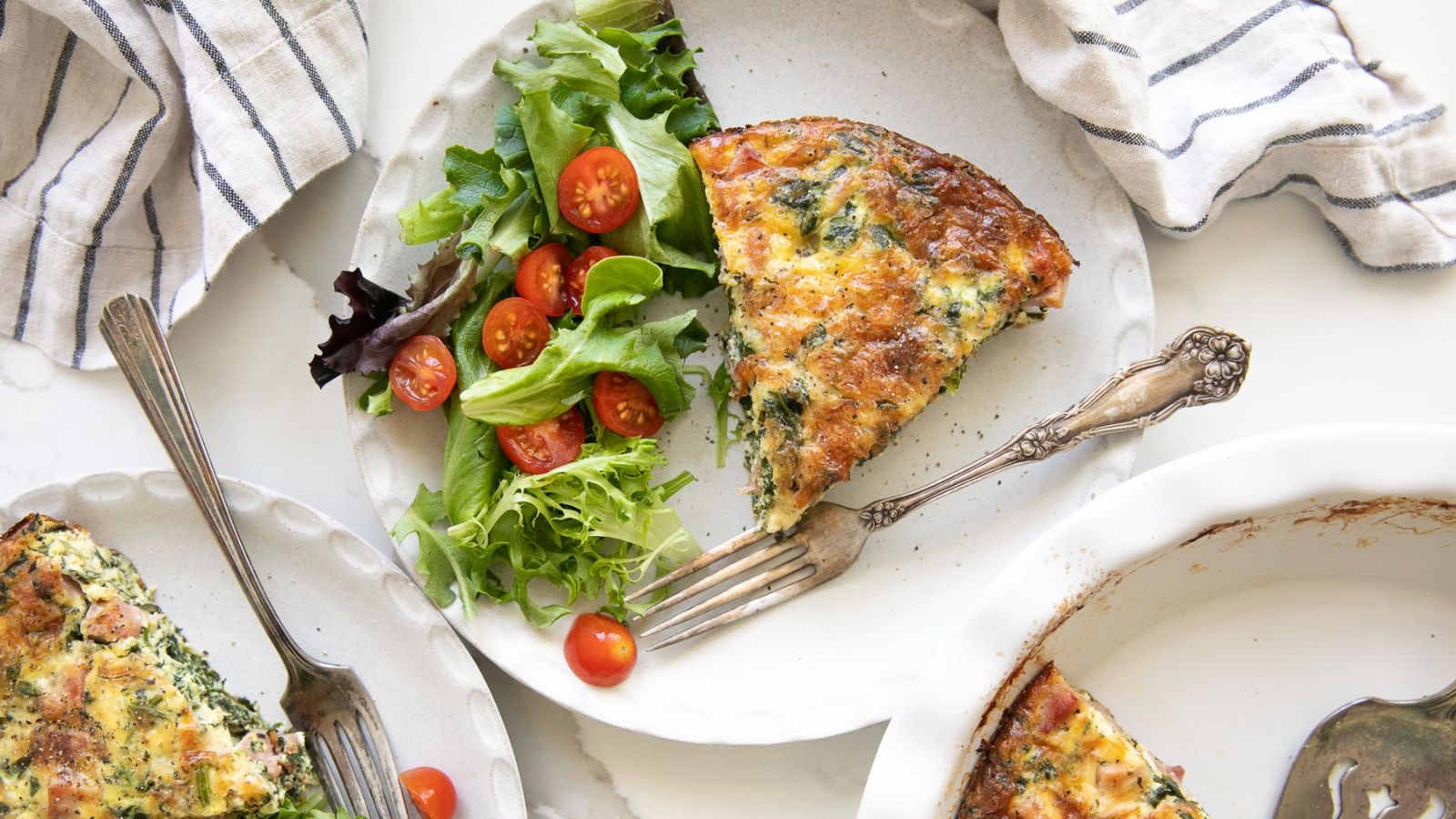 A slice pf spinach quiche with veggies on the side.