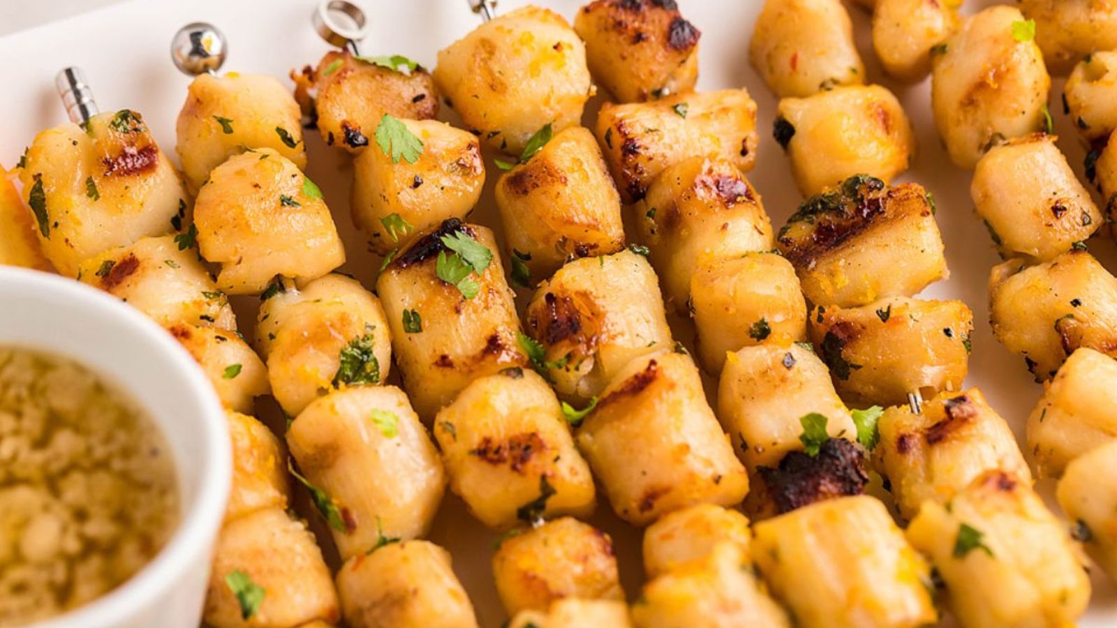 Grilled scallop skewers with dip on the side.