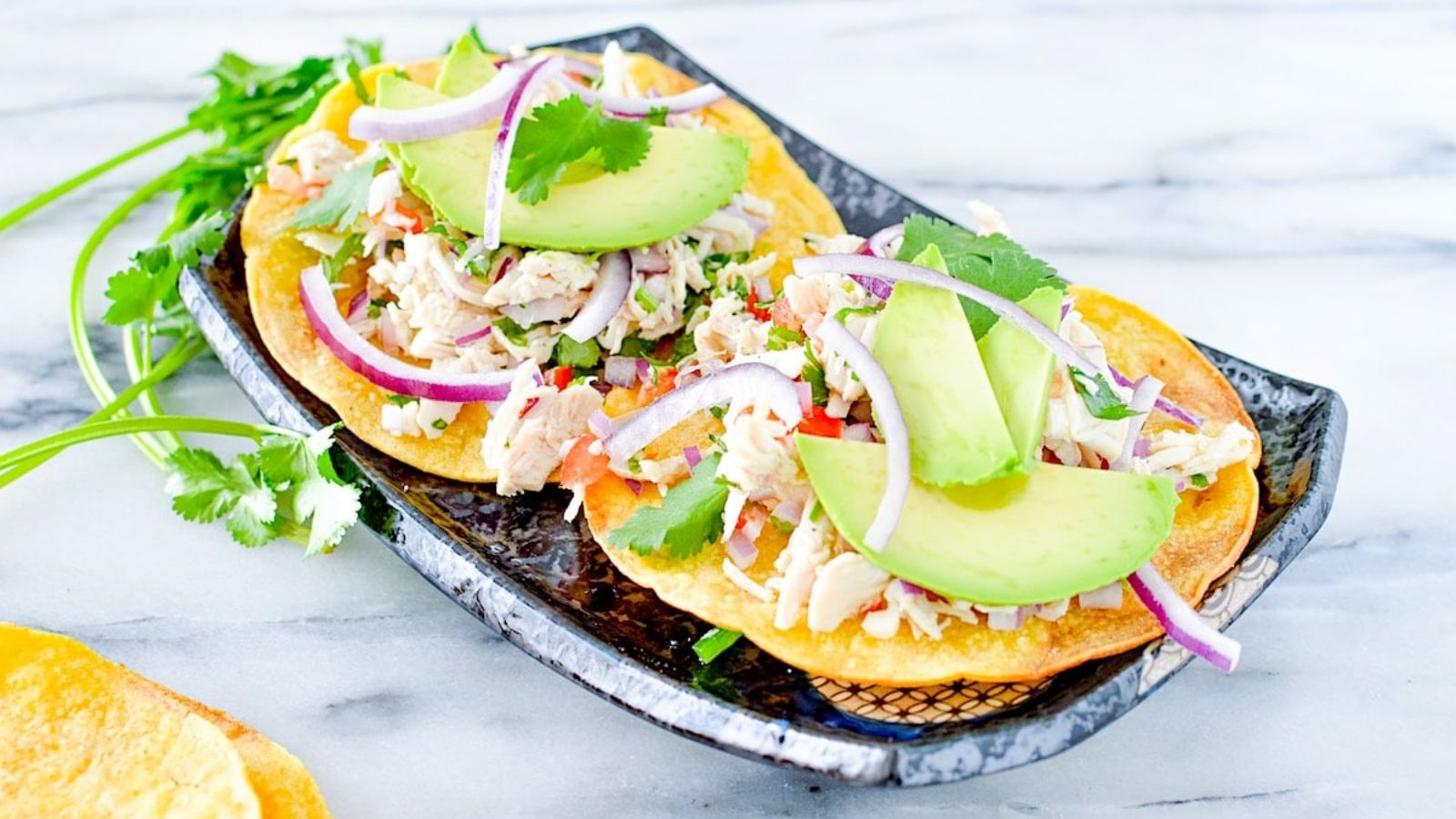 Two chicken salad tostadas with sliced avocados.