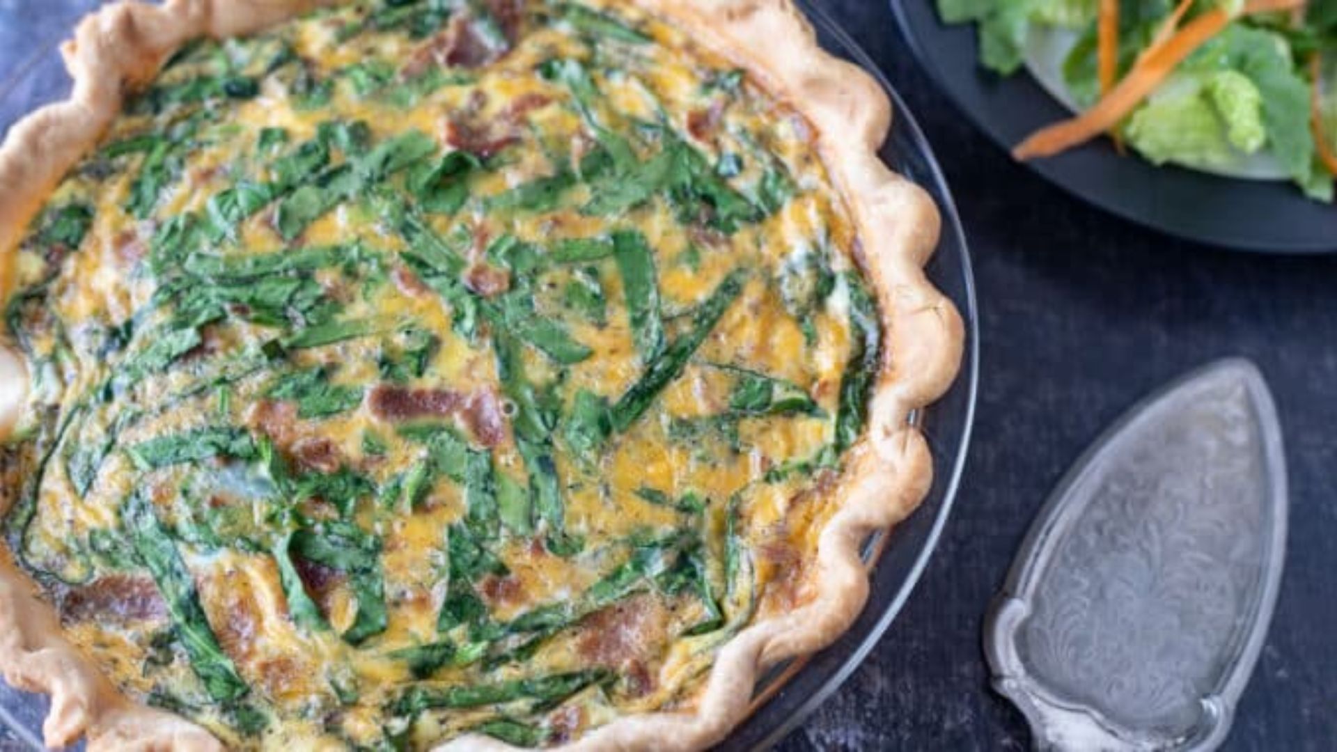 Whole quiche on a black board with antique pie server.