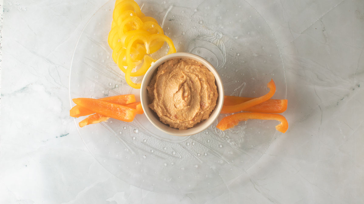 Hummus in a bowl with a few vegetables added to start assembly.