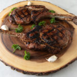 2 pork tomahawks on a board made from a slab of wood.
