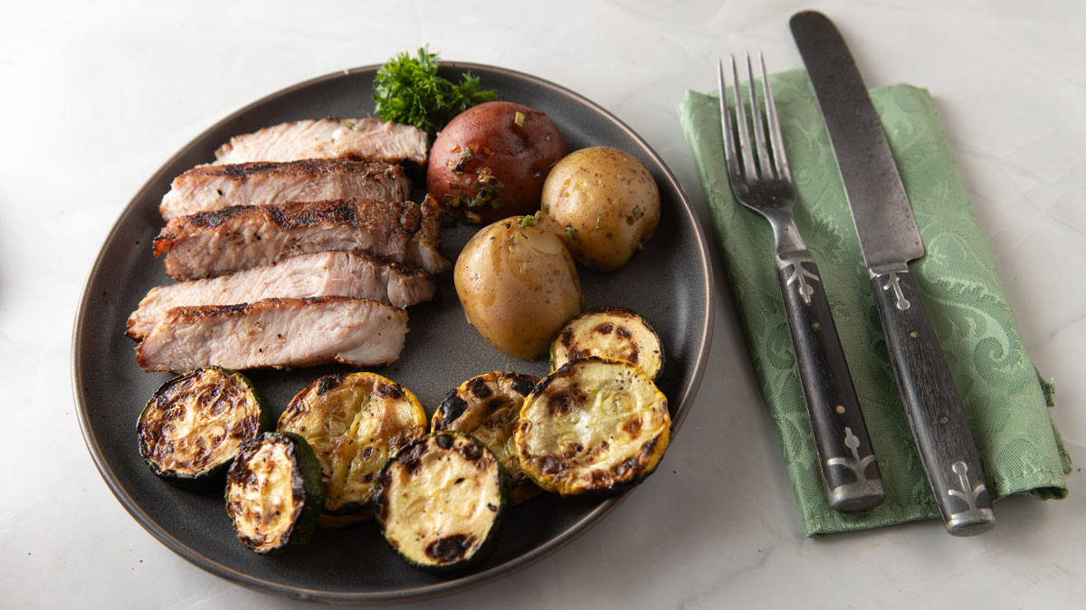 Slice of pork with side dishes on a gray plate.