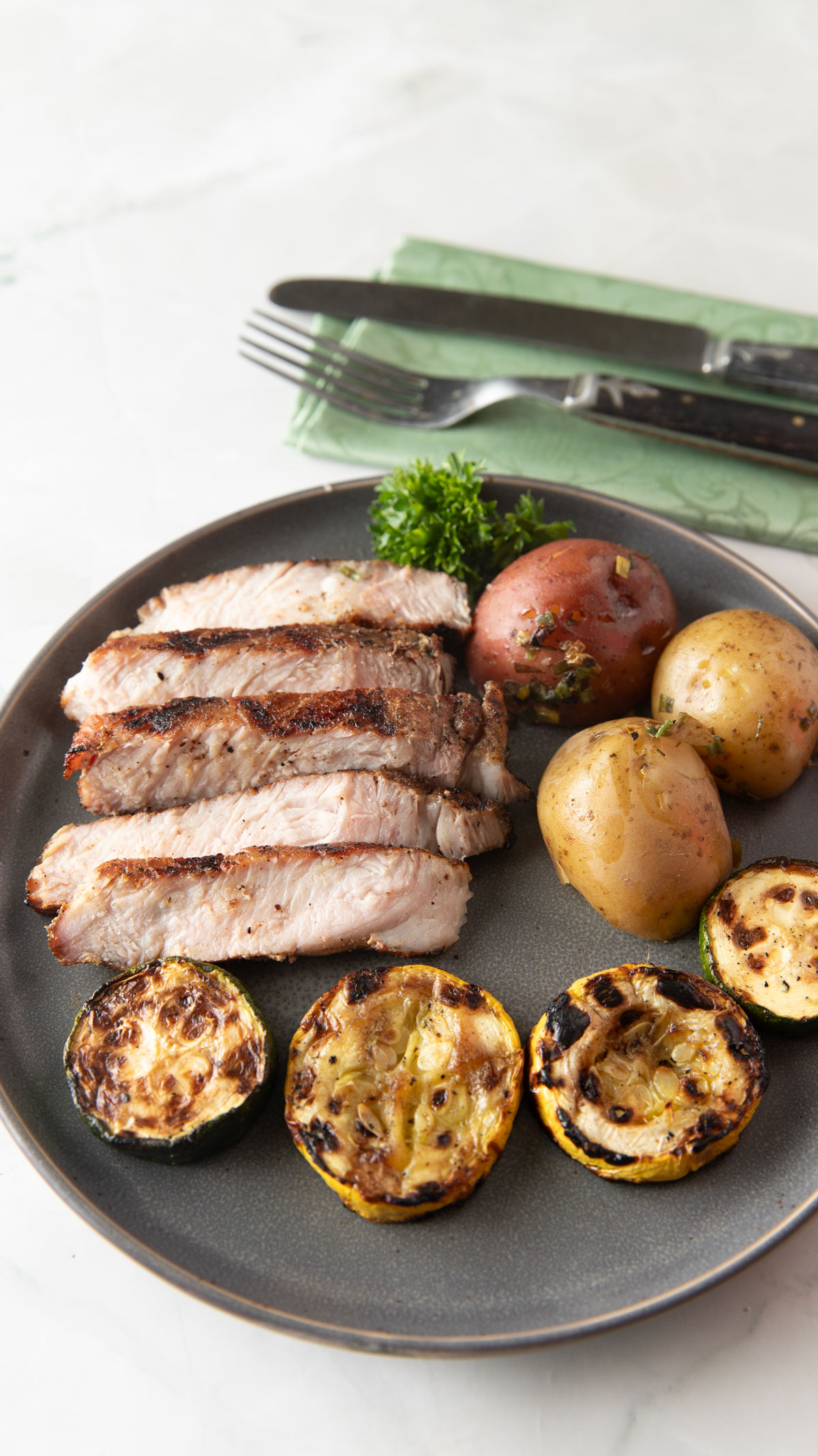 Slice pork on a gray plate with baby potatoes and roasted squash.