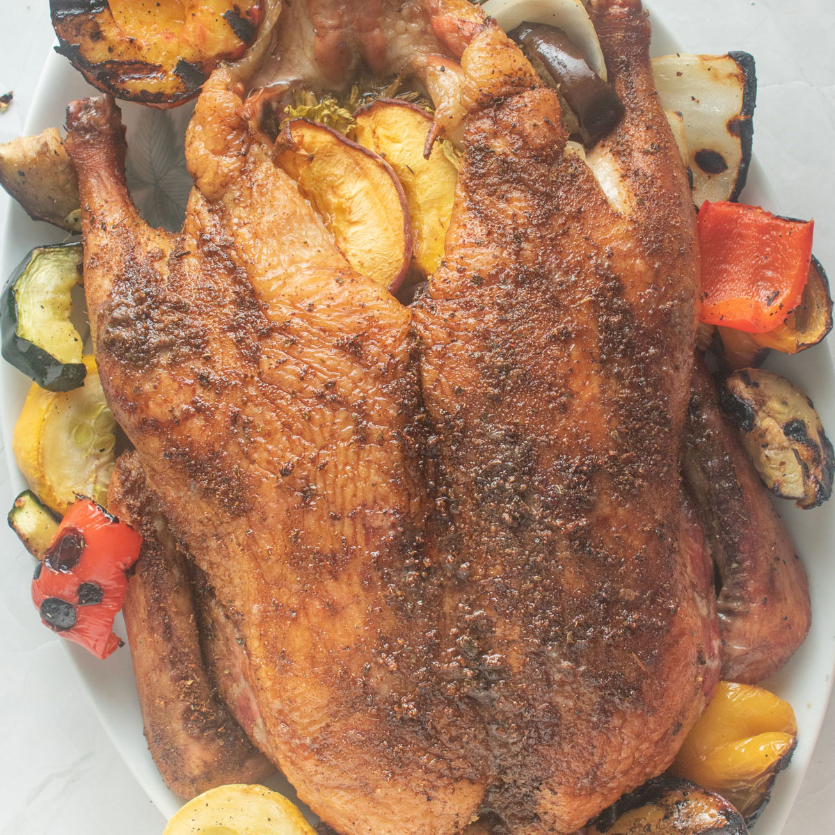 Whole duck on a platter with smoked vegetables around it.