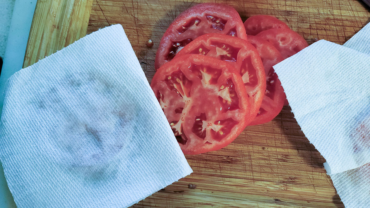 Patting sliced tomatoes with paper towels to absorb excess liquid.