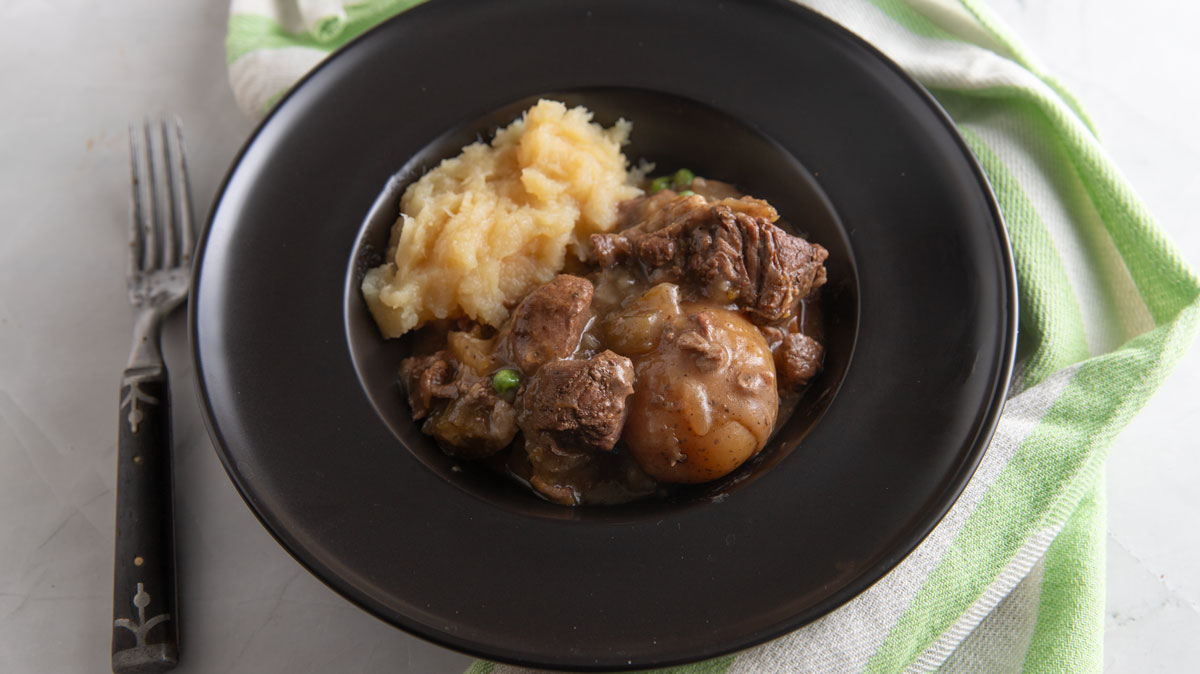 Beef stew in a black bowl with mashed squash.