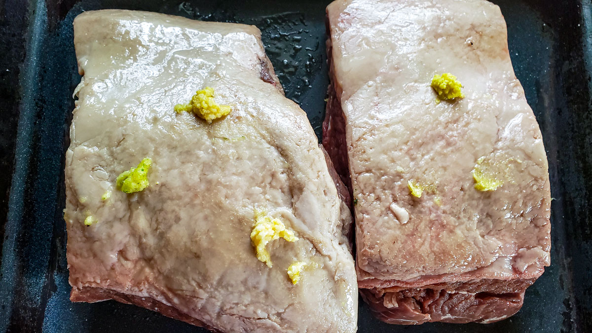 Spreading roasted garlic onto the meat.
