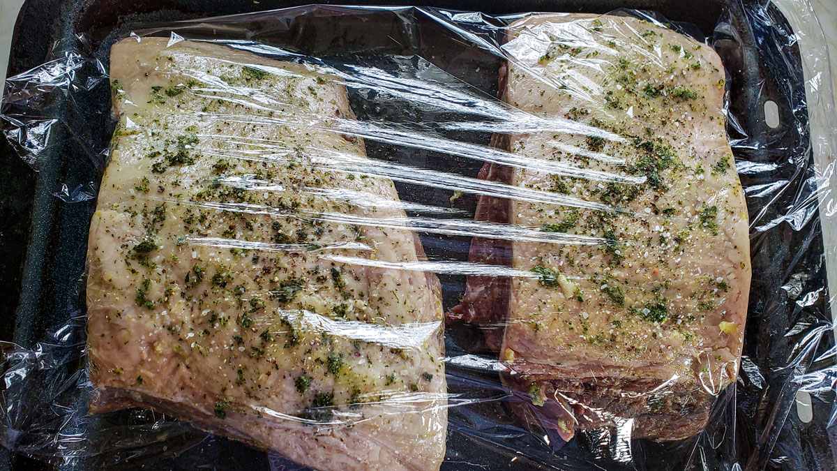 Plastic wrap coverering the baking sheet with the meat on it.