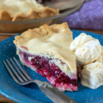 Slice of blackberry pie with scoops of ice cream on a blue plate.