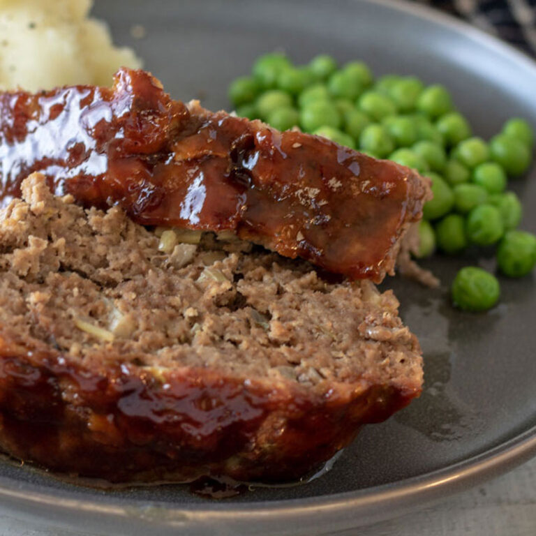 Two slices of meatloaf with mashed potatoes and peas on a gray plate.