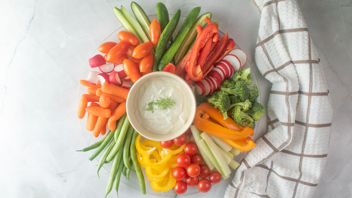 Colorful veggie tray with dill dip in a bowl in the center.