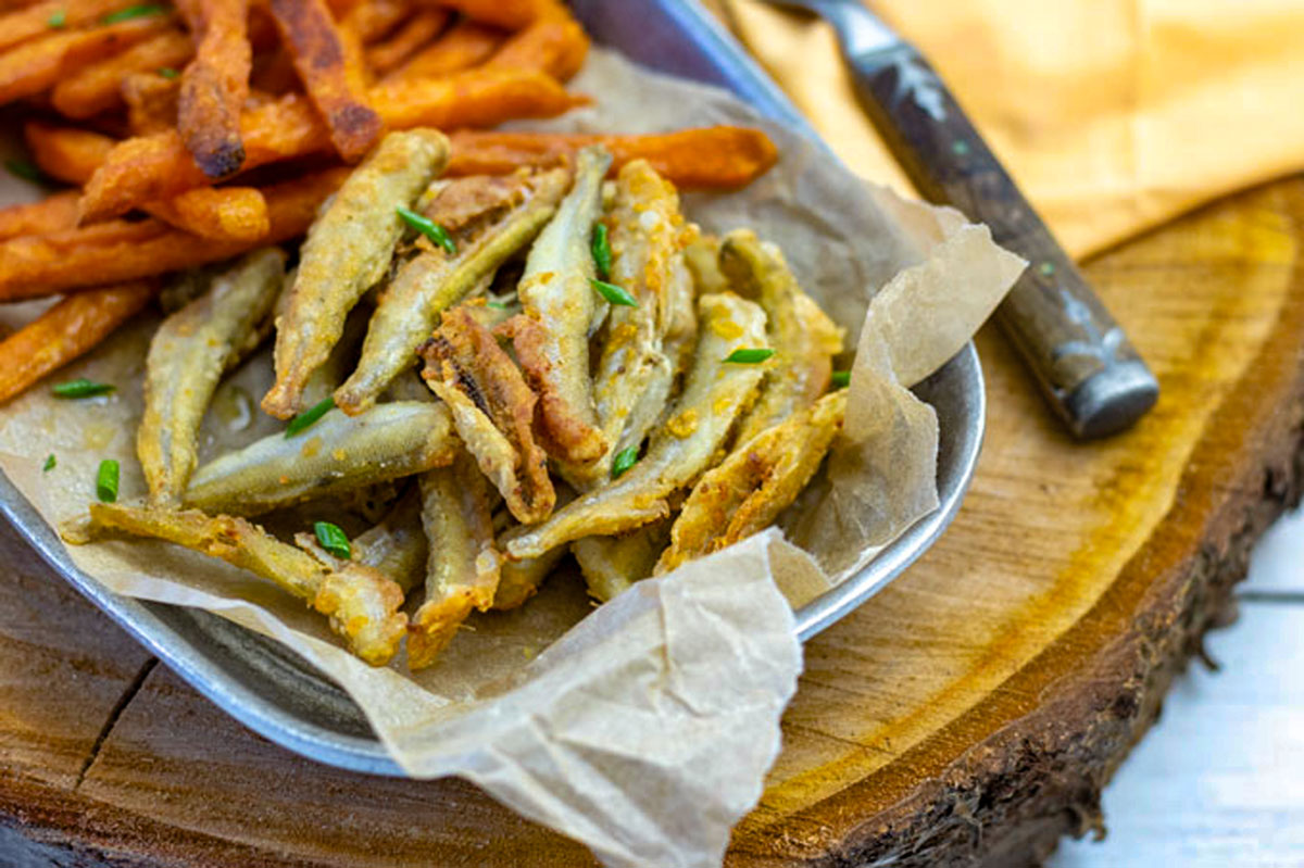 Crispy smelt on a log round in a bowl with sweet potato fries.