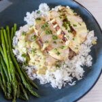 Sliced chicken breast on a bed of rice with curry sauce and asparagus on the side.