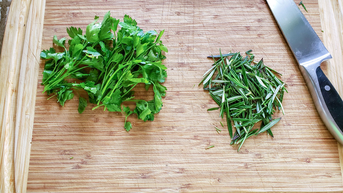 Fresh rosemary and parsley on a cutting board.