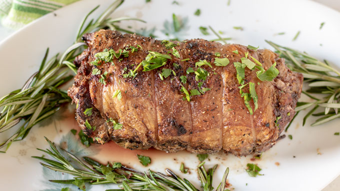 Whole lamb loin golden brown on a white platter with rosemary.