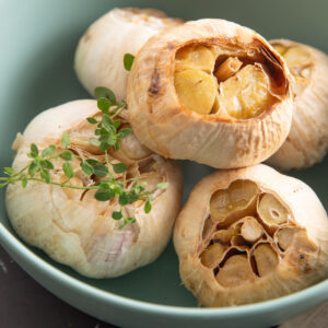 Whole heads of roasted garlic in a green bowl with a sprig of thyme.