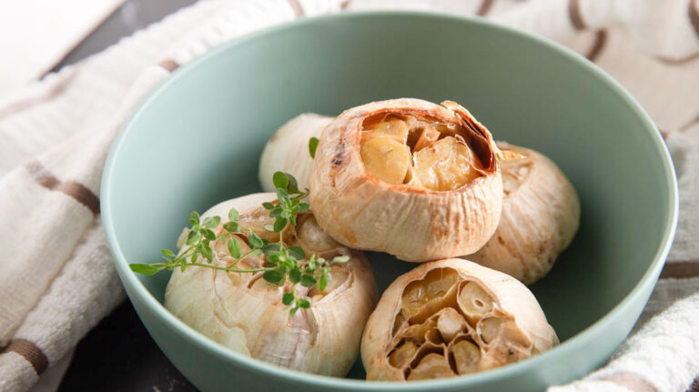 Whole heads of roasted garlic in a green bowl.