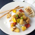 Colorful sweet and sour chicken with pineapple and red pepper on a white plate.
