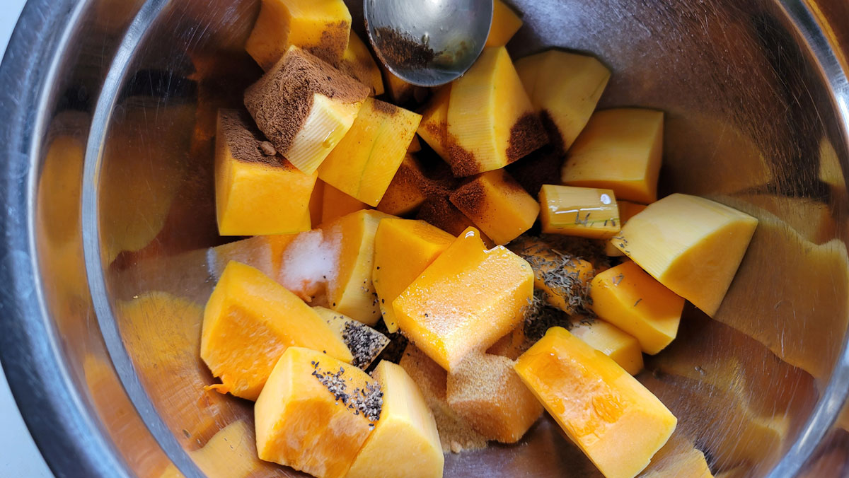 Squash cut into cubes and spices added to a bowl.