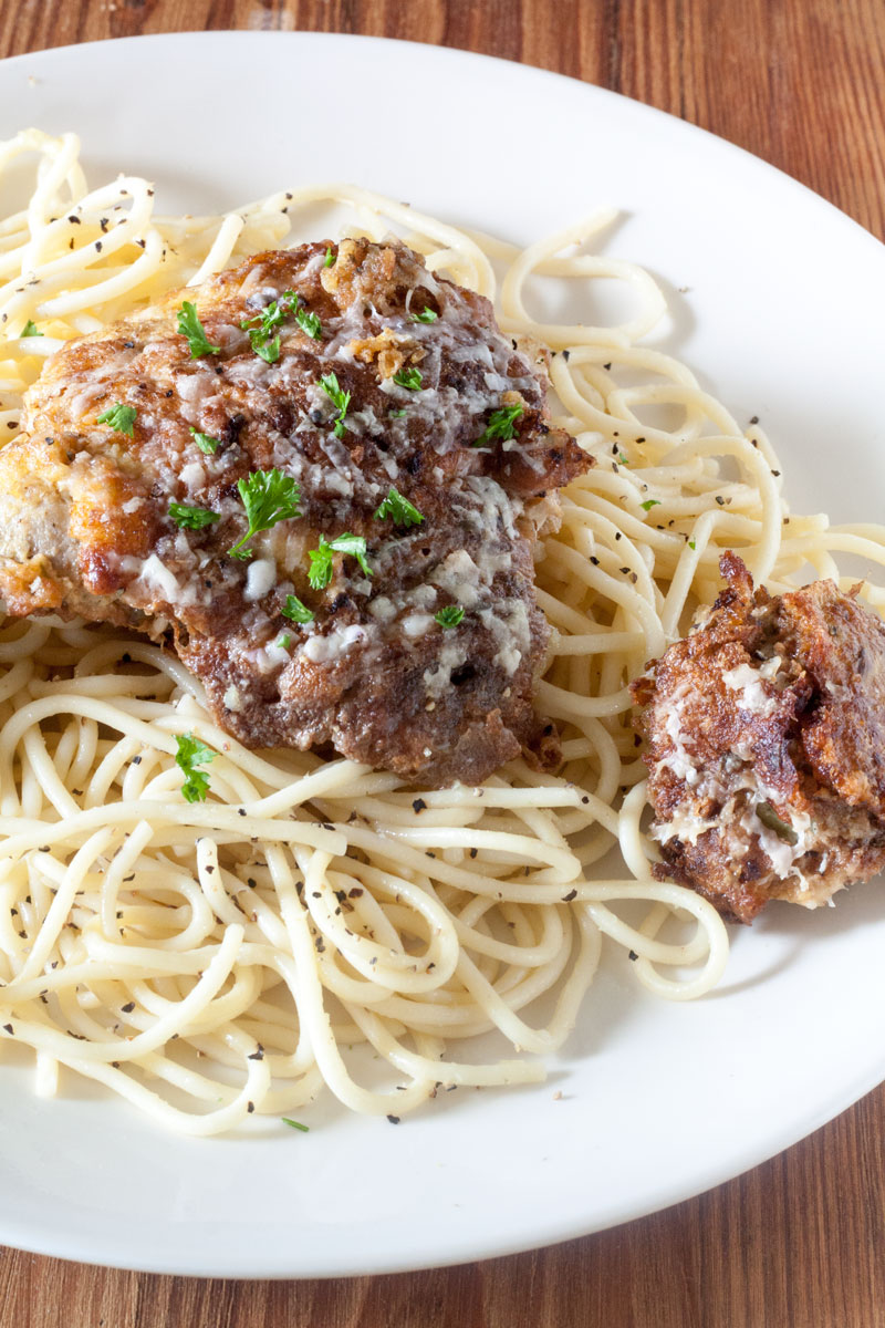White plate filled with pasta topped with chicken and artichoke French.