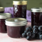 Jars of grape jam with fresh bundle of grapes.