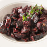 Close up of a white bowl filled with roasted beets with a thyme branch garnish.
