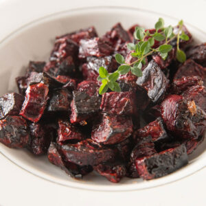 Close up of a white bowl filled with roasted beets with a thyme branch garnish.