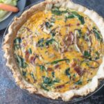 Whole quiche with bacon and spinach on a black board.