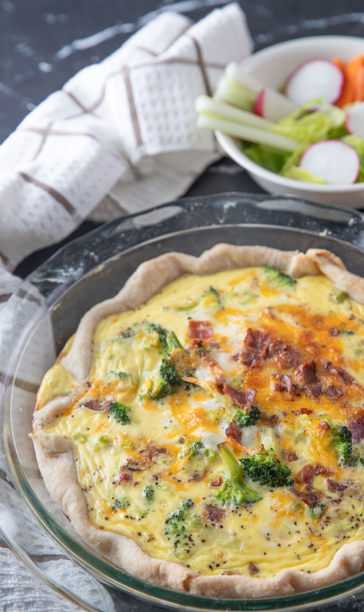 Whole quiche on black board with a salad in the background.