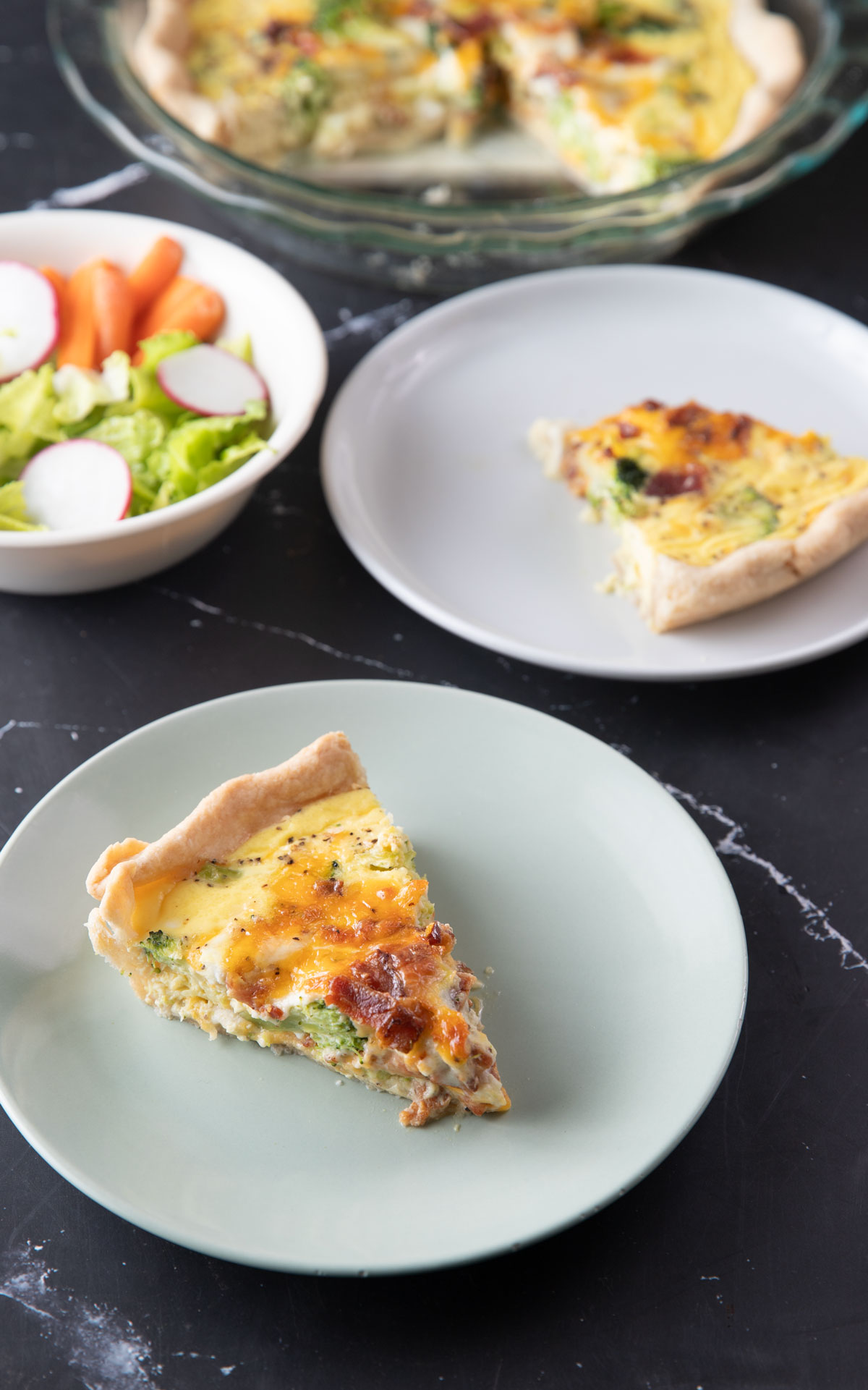 Slices of quiche on plate with a bowl of salad in the background.