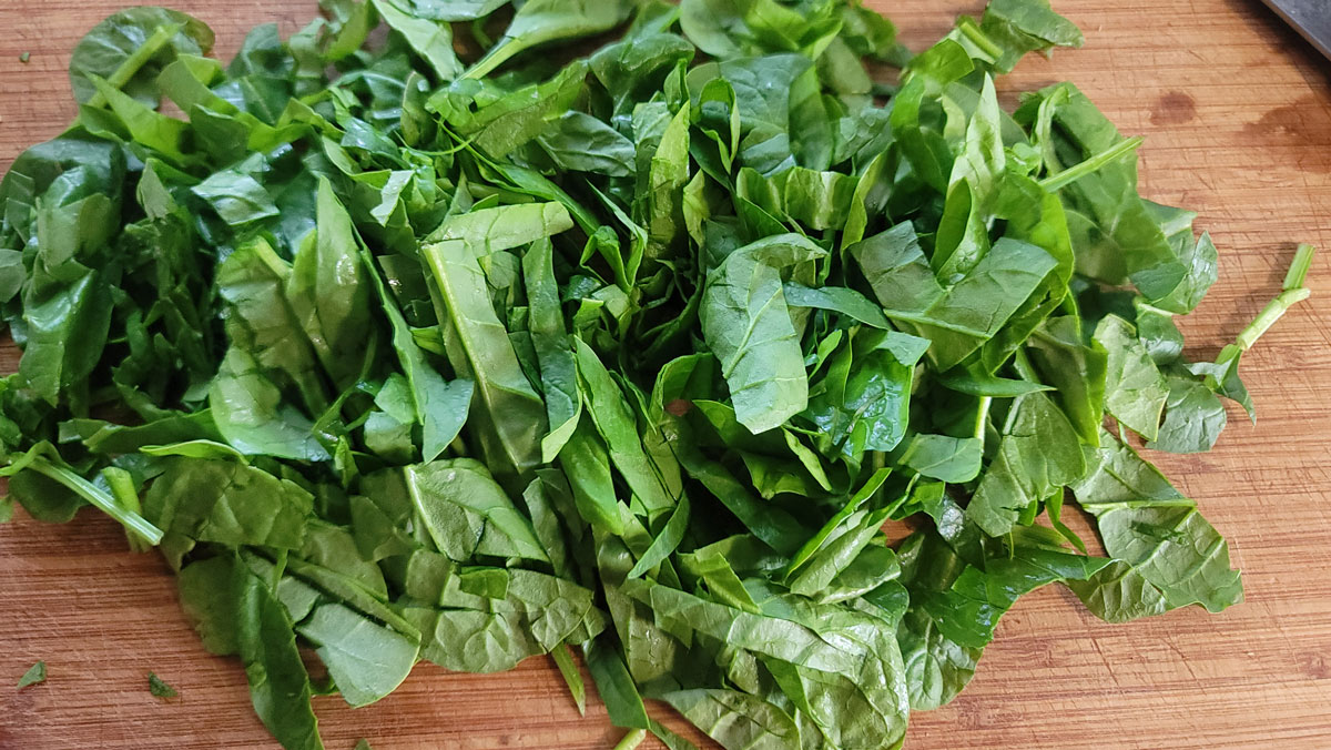Chopped spinach on a wooden cutting board.
