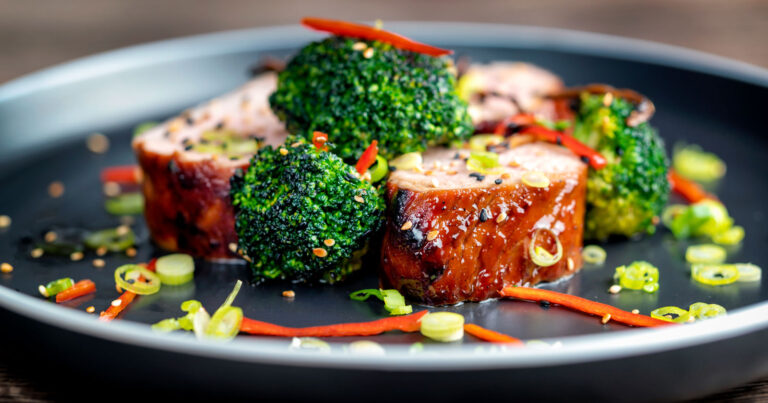 Side view of a colorful plate with pork slices and broccoli.