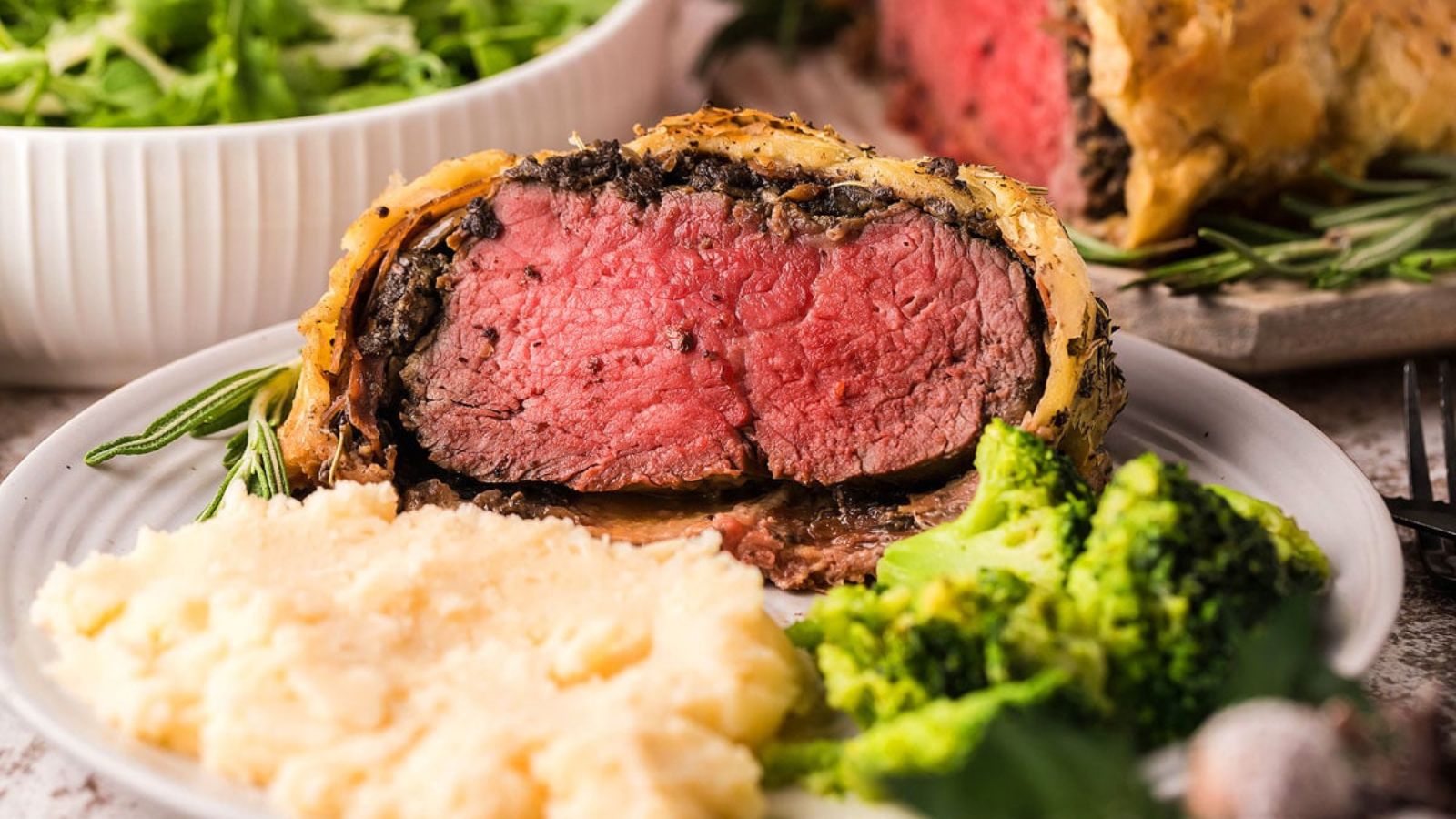 Close up of beef wellington with mashed potatoes and broccoli on the side.