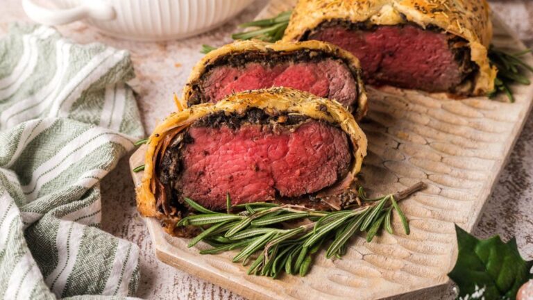 Slices of beef wellington on a cutting board garnished with fresh rosemary.